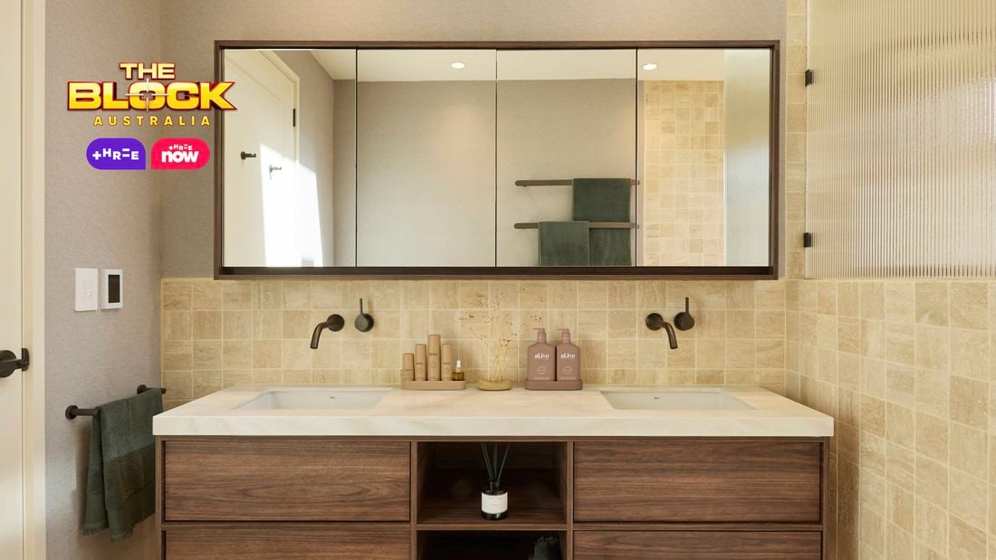 Modern bathroom with double sink vanity, large mirror, light tiles, glass shower partition, and white door with black hardware. 