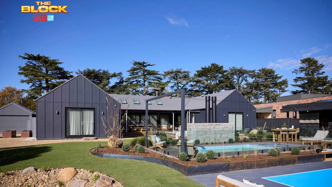 The back of a house with a pool in it, outdoor lounge, rocks area and an outdoor fireplace in it.