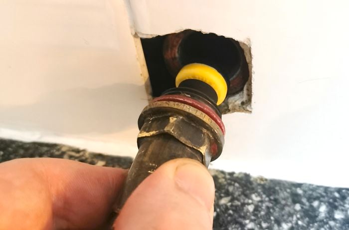 A hand screwing a spindle back into a tap bonnet.