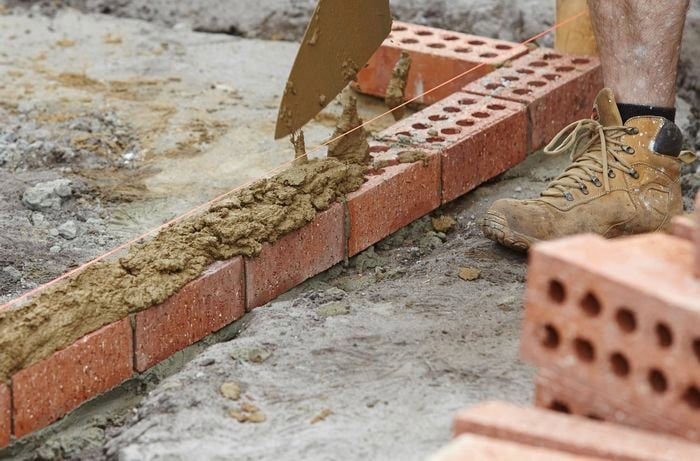 Person scraping mortar on top of row of bricks.