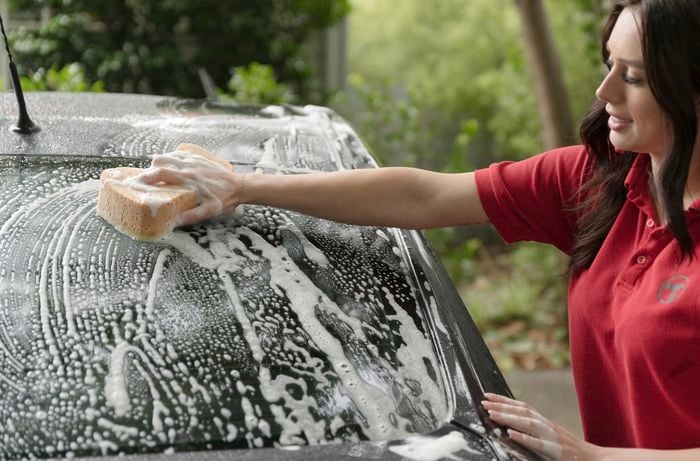 A cheerful Bunnings team member is using a sponge to wash the car with soapy water.