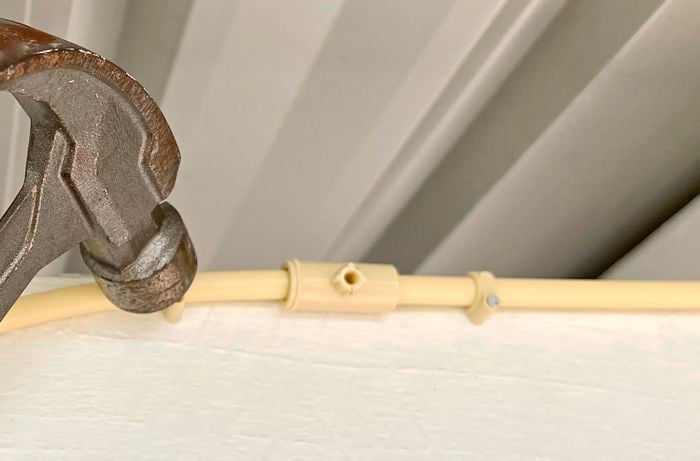 A person using a hammer to attach a misting pipe assembly to a wall
