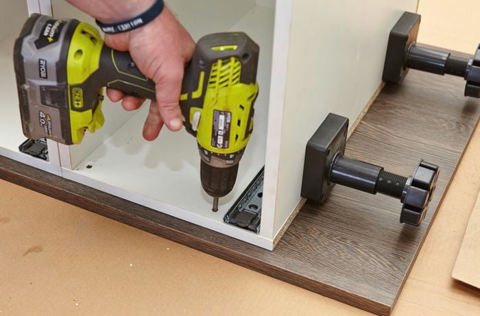 A person attaching cabinets to side panel using a cordless driver