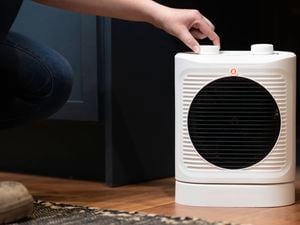 A person is adjusting the thermostat on a 2400W fan heater.