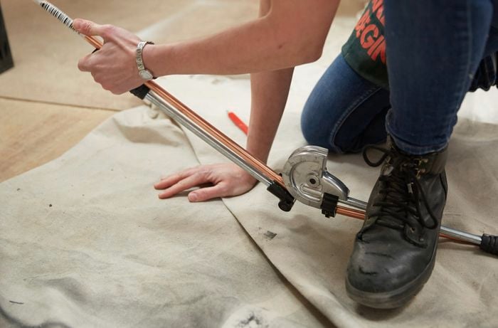 Person using pipe bender to bend copper piece