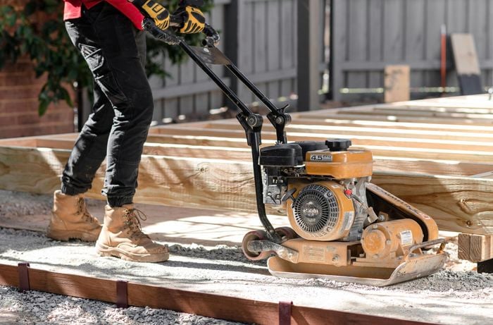 Person using a compactor on a gravel base.