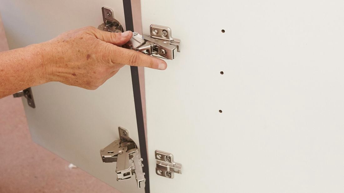 A person fitting hinges to a cabinet door