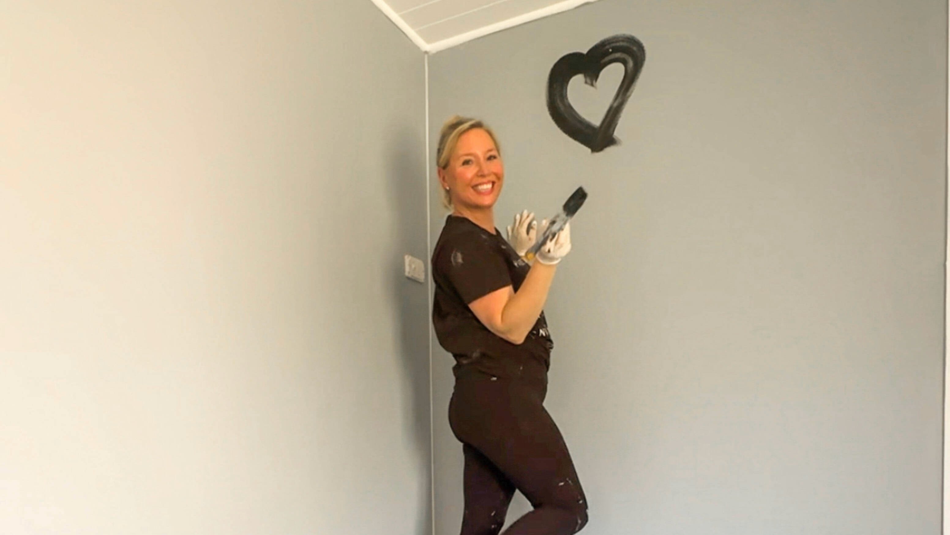 Person standing on a ladder with a paint brush and a heart painted on the wall