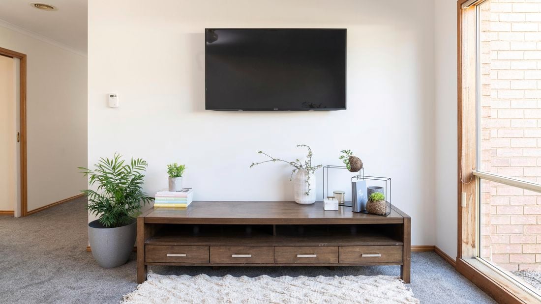 Living room with TV hanging on well, brown entertainment unit, plant, and other decorative items.