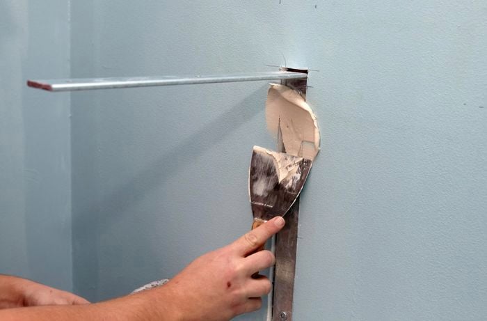 A person filling a vertical gap in a wall using a paint scraper