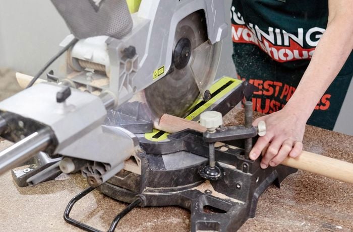 A mitre saw being used to cut a piece of dowel by a Bunnings team member