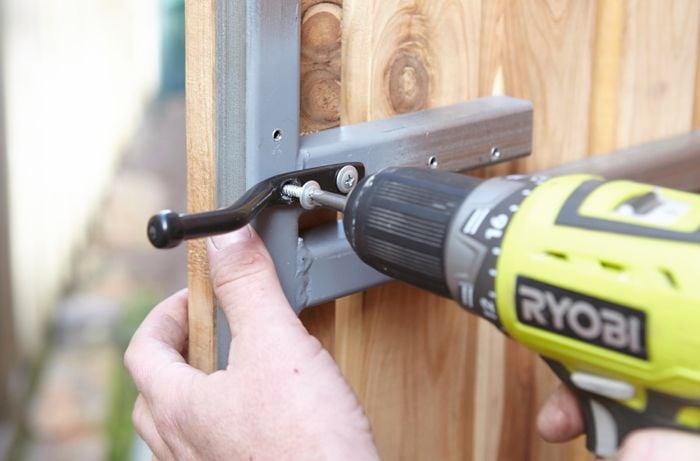 Person drilling gate latch into fence.