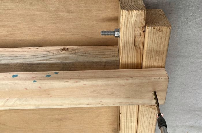A drill driving a screw into a brace attached to a larger timber assembly.