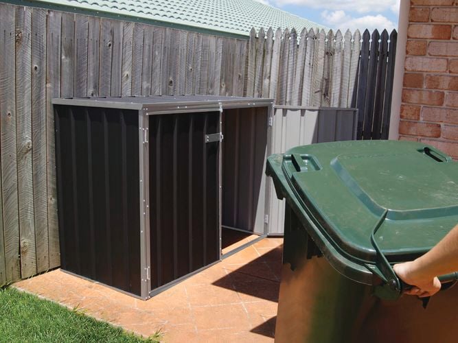 A person moving a wheelie bin from a bin shed.