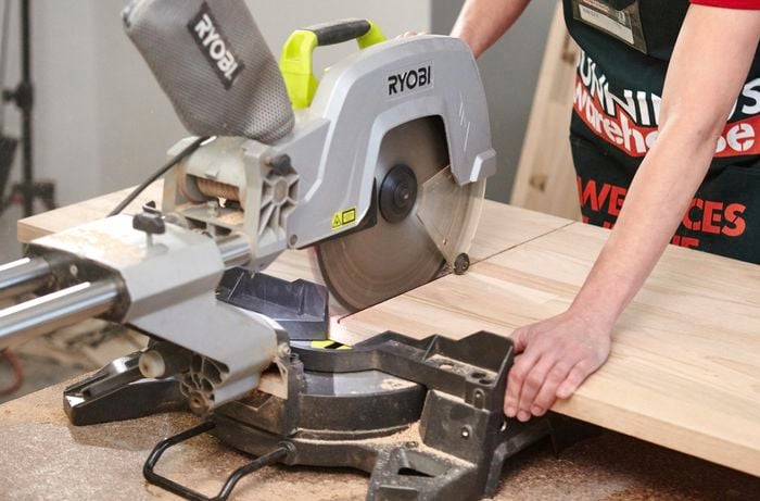 A person cutting a timber panel using a drop saw