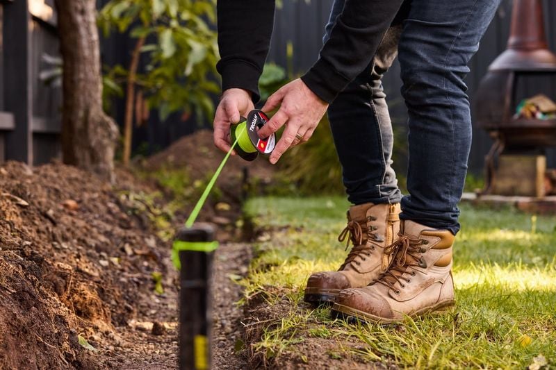 Person with denim jeans and boots standing on grass, measuring part of the ground