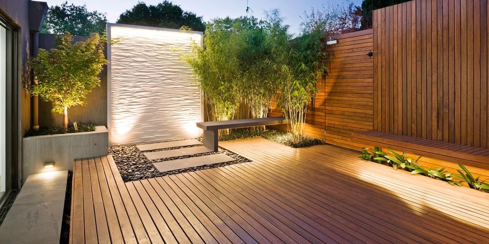 Timber decking and decorative ripple standing feature with surrounding pebbles, pavers and small trees.