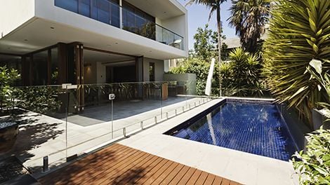 A pool behind a multi-storey property, fenced off by clear glass panels