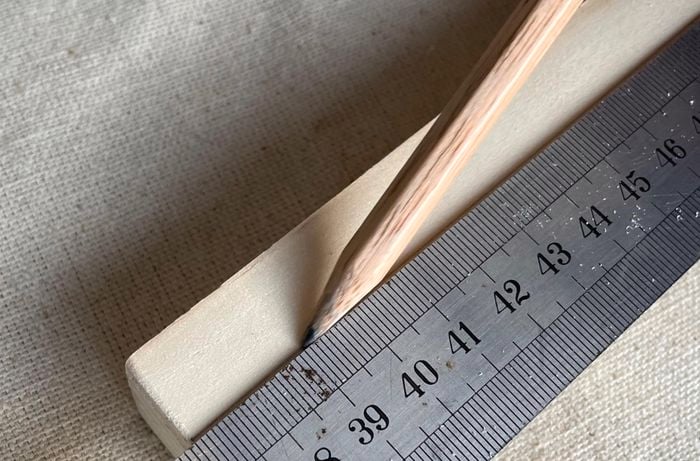 A person uses a ruler to mark the halfway point on a pine piece.