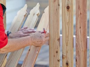 Person marking spacing between pickets leaning against fence rail