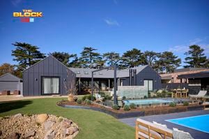 The back of a house with a pool in it, outdoor lounge, rocks area and an outdoor fireplace in it.