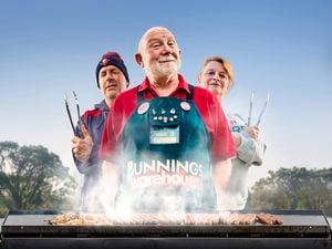 A Bunnings Team Member and 2 people in front of a BBQ with food on top of it.