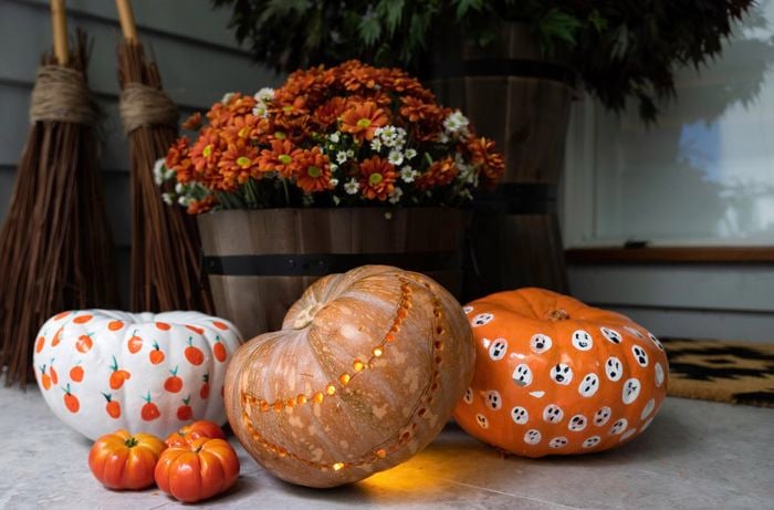 Three decorated pumpkins in front of a potted plant in a barrel.