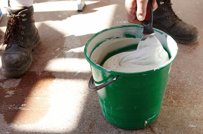 Person mixing up plaster in bucket using scraper.