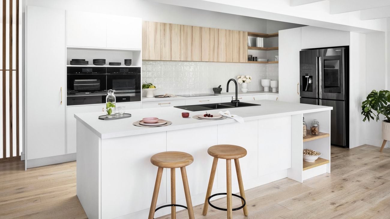 A spacious modern kitchen with white cupboards, steel appliances, shelving, an extended wooden island with bar stools, and other decor