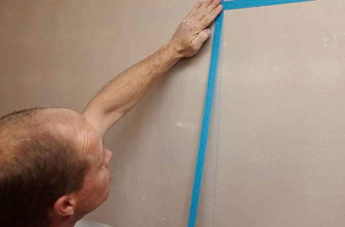 A person applying masking tape to a bathroom wall