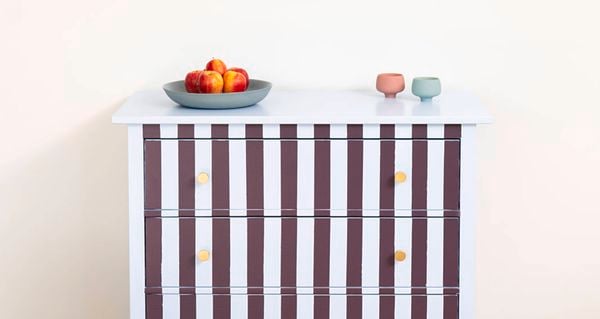 Small cabinet with vertical burgundy and white stripes, photographed front-on against a plain wall.