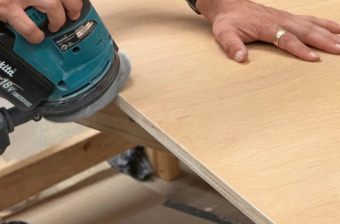  A hand using a sander to smooth the surface of a piece of plywood.