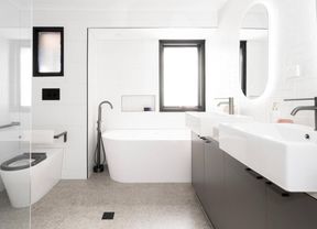A white bathroom with a bath, two sinks and a toilet fitted with accessibility features.]