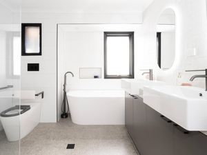 A white bathroom with a bath, two sinks and a toilet fitted with accessibility features.]