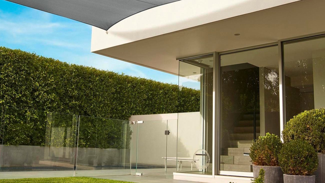 The backyard of a house with glass windows and a shade covering some of the yard.