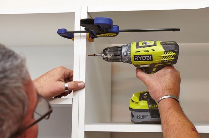 Using a clamp and drill to secure the cabinets in the linen closet