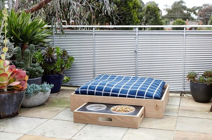 An outdoor area with a boxed dog bed and boxed dog food bowls