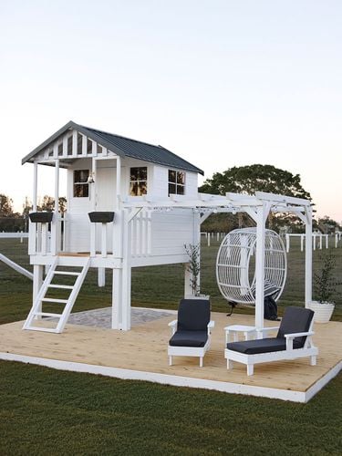Elevated children's playhouse painted white with gable roof, pergola and chair swing
