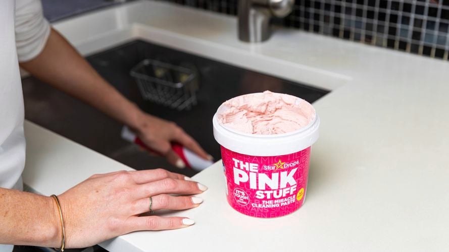 A tub of The Pink Stuff sitting on a white marble benchtop next to a sink.