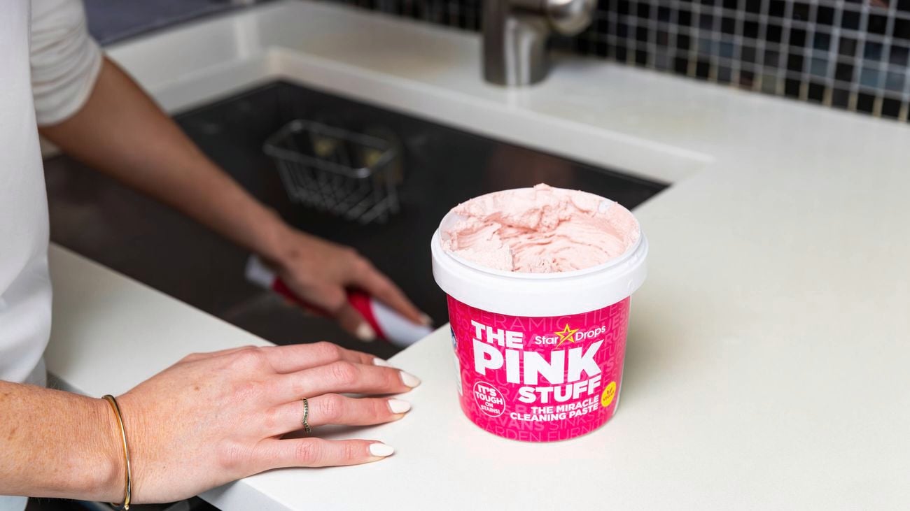 A tub of The Pink Stuff sitting on a white marble benchtop next to a sink.