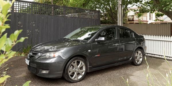 A steel grey Mazda SP23 is parked in the shade of a tree.