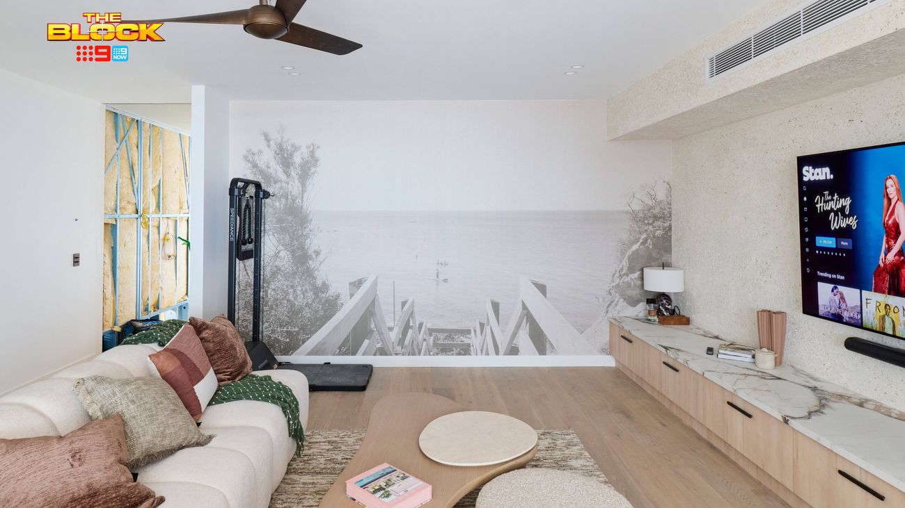 Contemporary living room featuring a neutral sofa, timber entertainment unit, wall-mounted TV, ceiling fan and large monochrome wall mural.