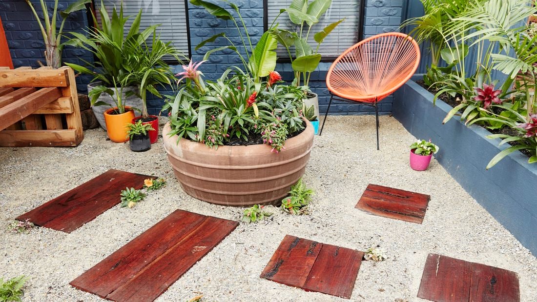 An outdoor area with timber pavers laid into white gravel amid potted plants