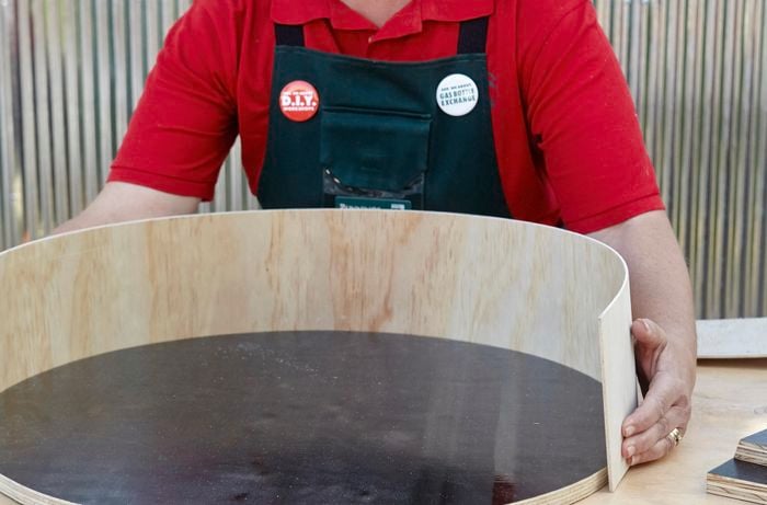 A person curving a strip of plywood around a circular plywood base
