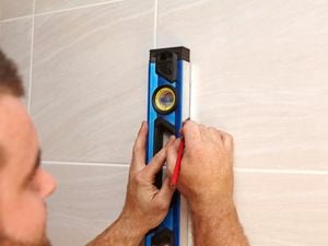 Person marking a tiled wall with a spirit level and pencil