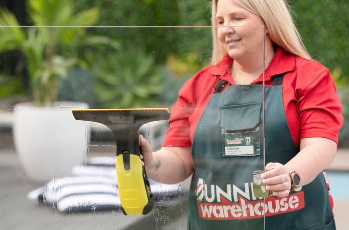 A Bunnings team member cleaning a pane of glass used in a pool fence with a squeegee