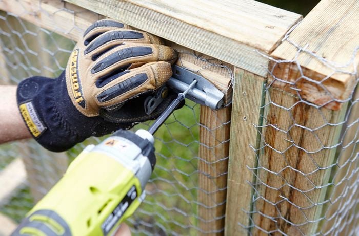 A slide lock being screwed into place on the door of a chicken coop by a Bunnings team member with a power drill