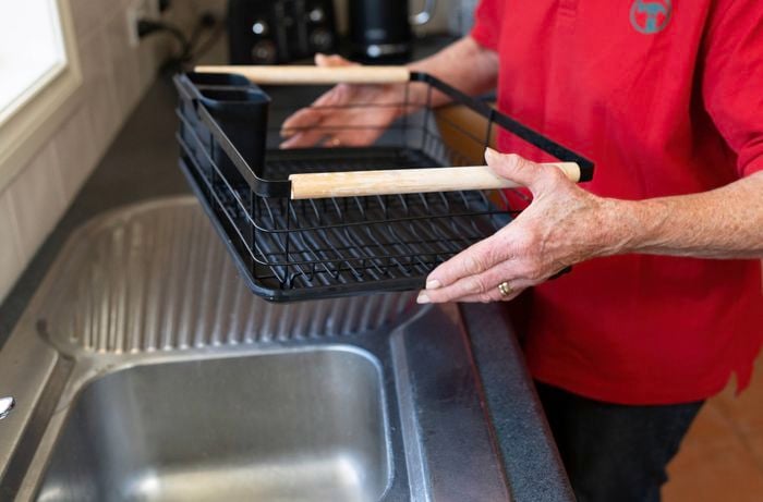  A Bunnings Team Member is holding a black dish rack with wooden handles over a kitchen sink. 
