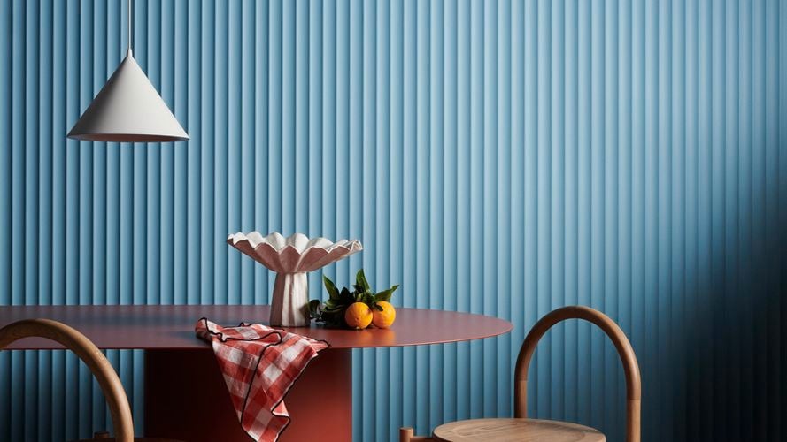 A hanging lamp, table and two chair in front of a blue Laminex wall.
