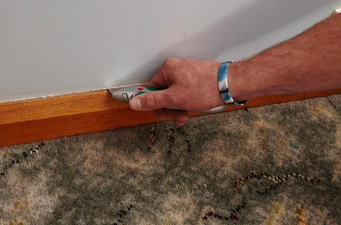 A person cutting along the top edge of a skirting board using a trimming knife